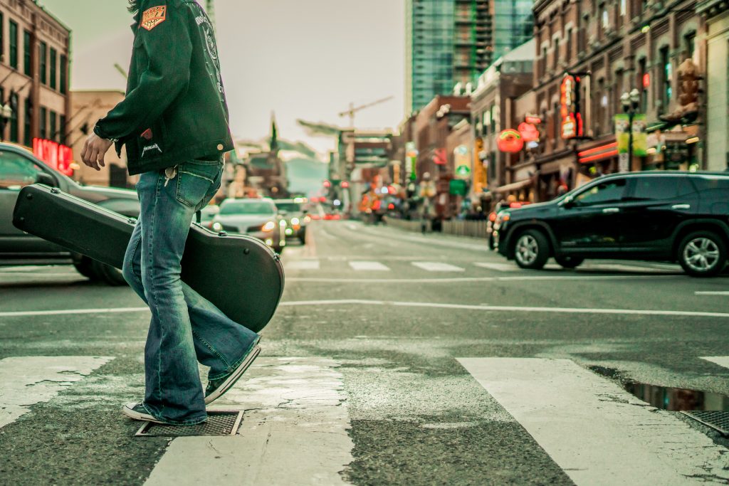 A man walking down the street in Nashville holding a guitar case. 