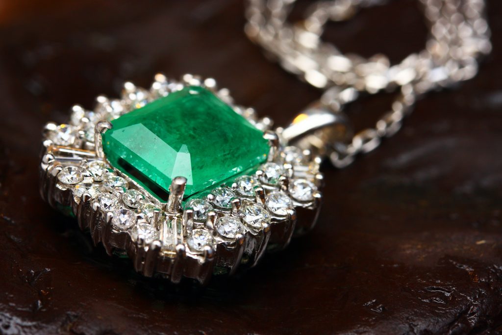 A silver necklace with diamonds surrounding a large emerald.