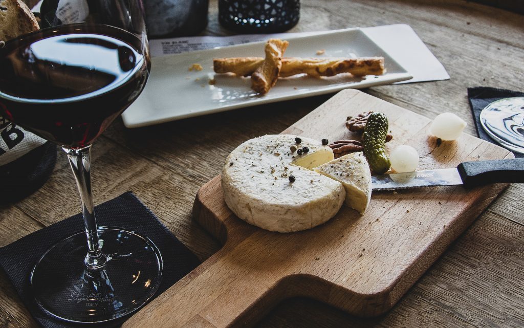 Read wine with a block of soft cheese and a pickle on a cutting board. 