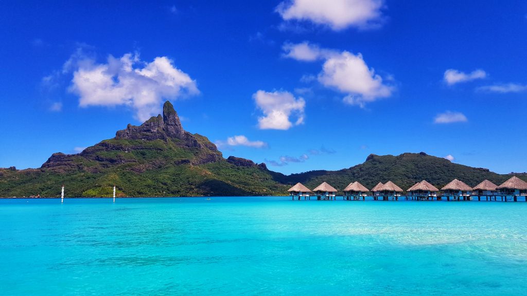 A mountain with overwater accommodation and the ocean in the foreground in Bora Bora.