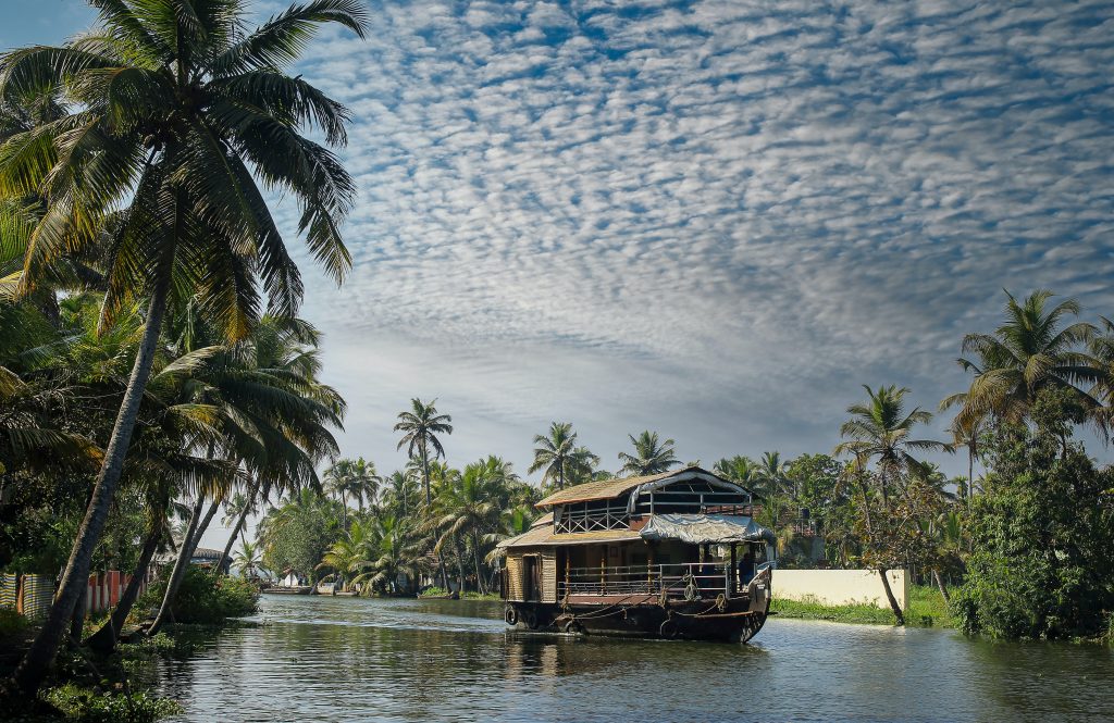 A houseboat sailing on a canal in Kerala under a sparsely clouded blue sky. 