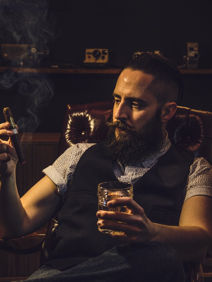 Man enjoying a cigar with his whiskey.