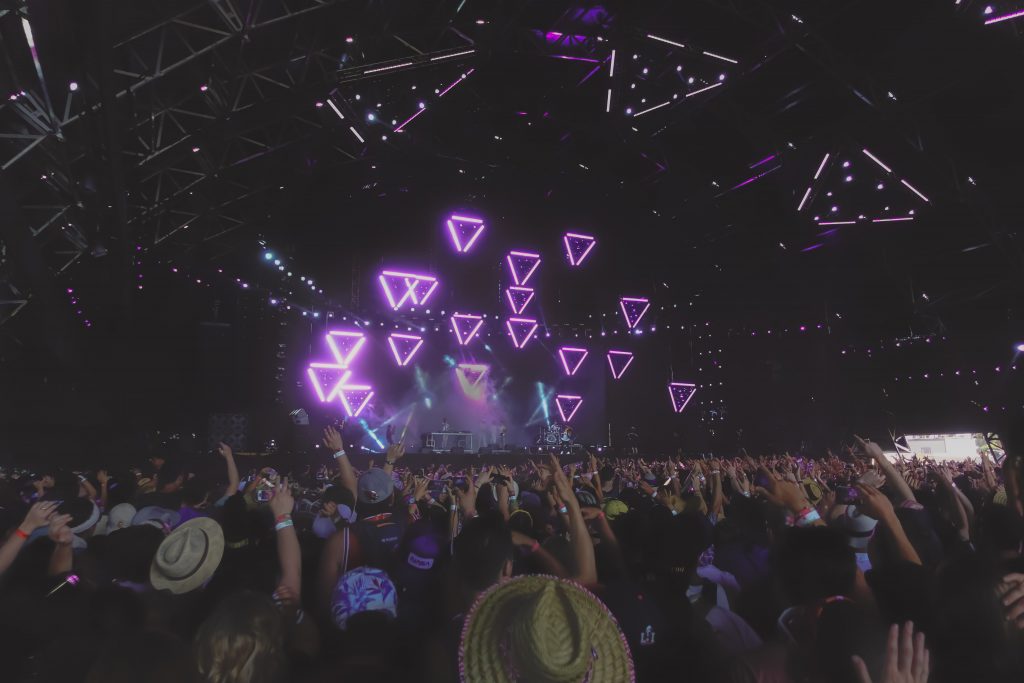 Coachella in the evening, Crowds in front of a stage with neon-purple triangles. 