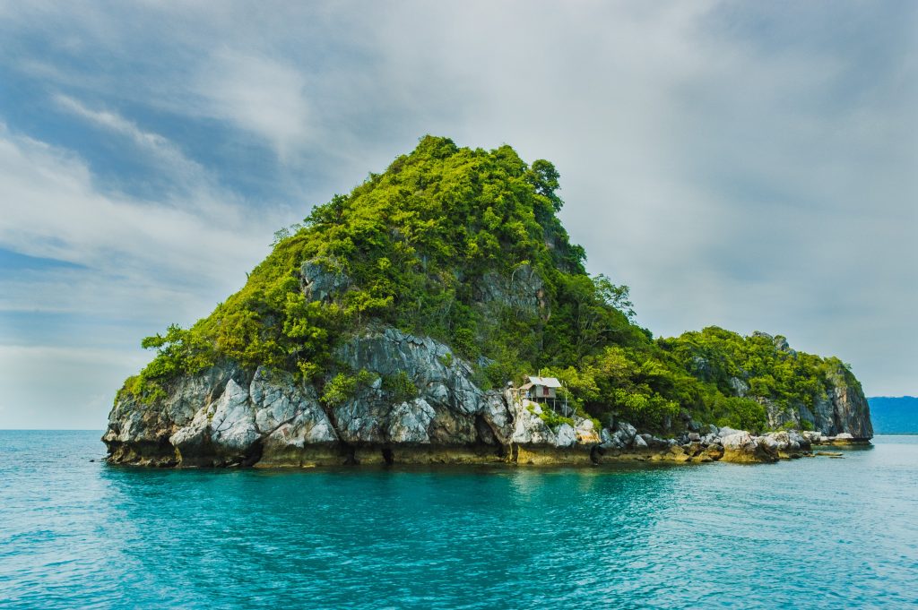 Thailand's south is known for its stunning landscape. A rock in the sea, covered in vegetation. 