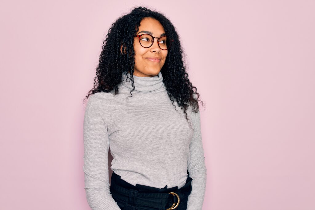 Young african american woman wearing turtleneck sweater and glasses over pink background smiling looking to the side and staring away thinking.